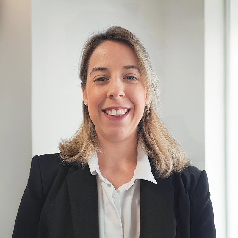 Portrait of Elena Cardin of Deserving Italy, smiling in a dark blazer and white shirt against a light wall.