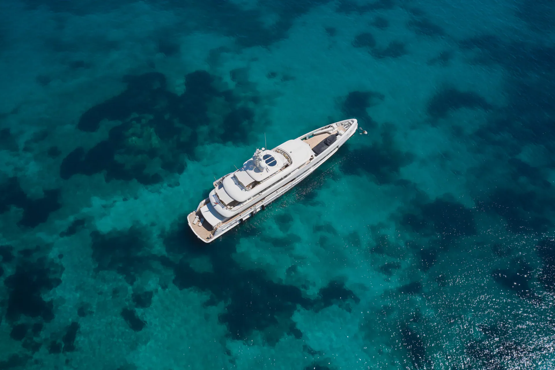Top-down aerial drone shot of a large white luxury superyacht anchored alone in the middle of a stunning turquoise and deep blue sea, revealing the seabed textures below. Likely location: Costa Smeralda, Sardinia.