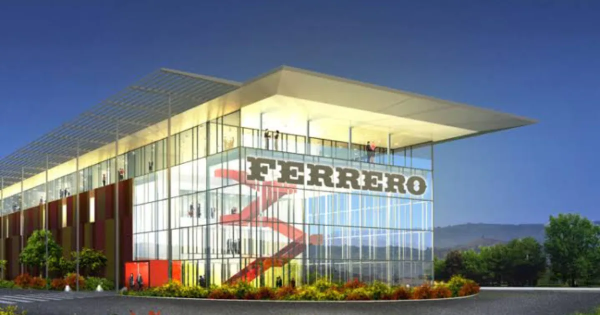 The glass-fronted Ferrero building in Alba lit at dusk, the company born from the hazelnut groves of the Langhe.