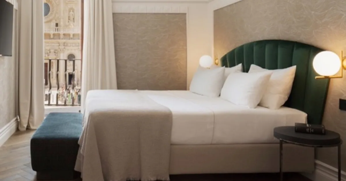 A hotel room at Patria Palace in Lecce with a green velvet headboard and a balcony opening onto the baroque facade of Santa Croce.