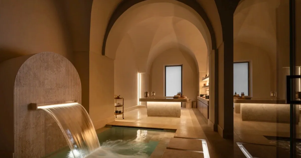 The vaulted stone spa at Patria Palace in Lecce, where a sheet of water falls into a small plunge pool under warm lighting.