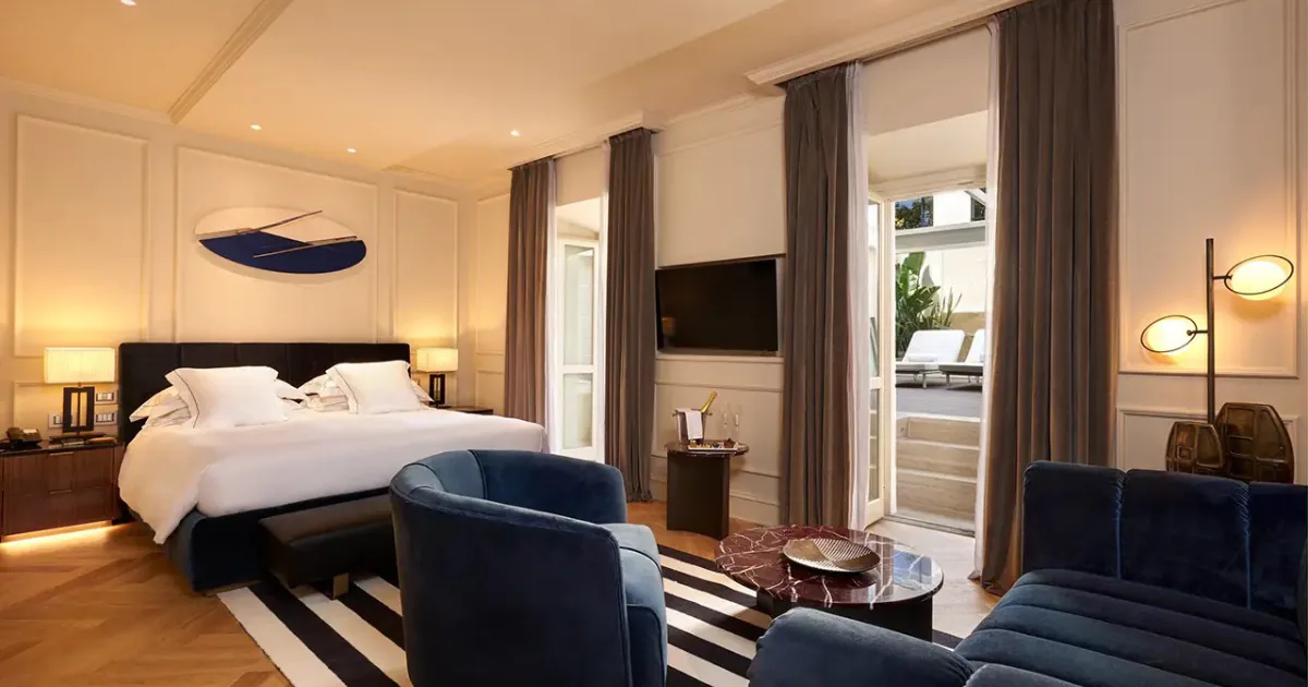 A contemporary room at The First Arte in Rome, with blue velvet armchairs, a striped rug and glass doors opening onto a private terrace.