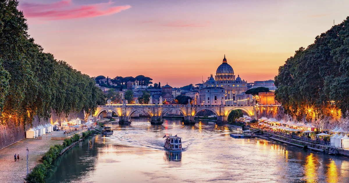 The Tiber at dusk, with Ponte Sant'Angelo crossing the river and the dome of St Peter's rising against a pink sky.