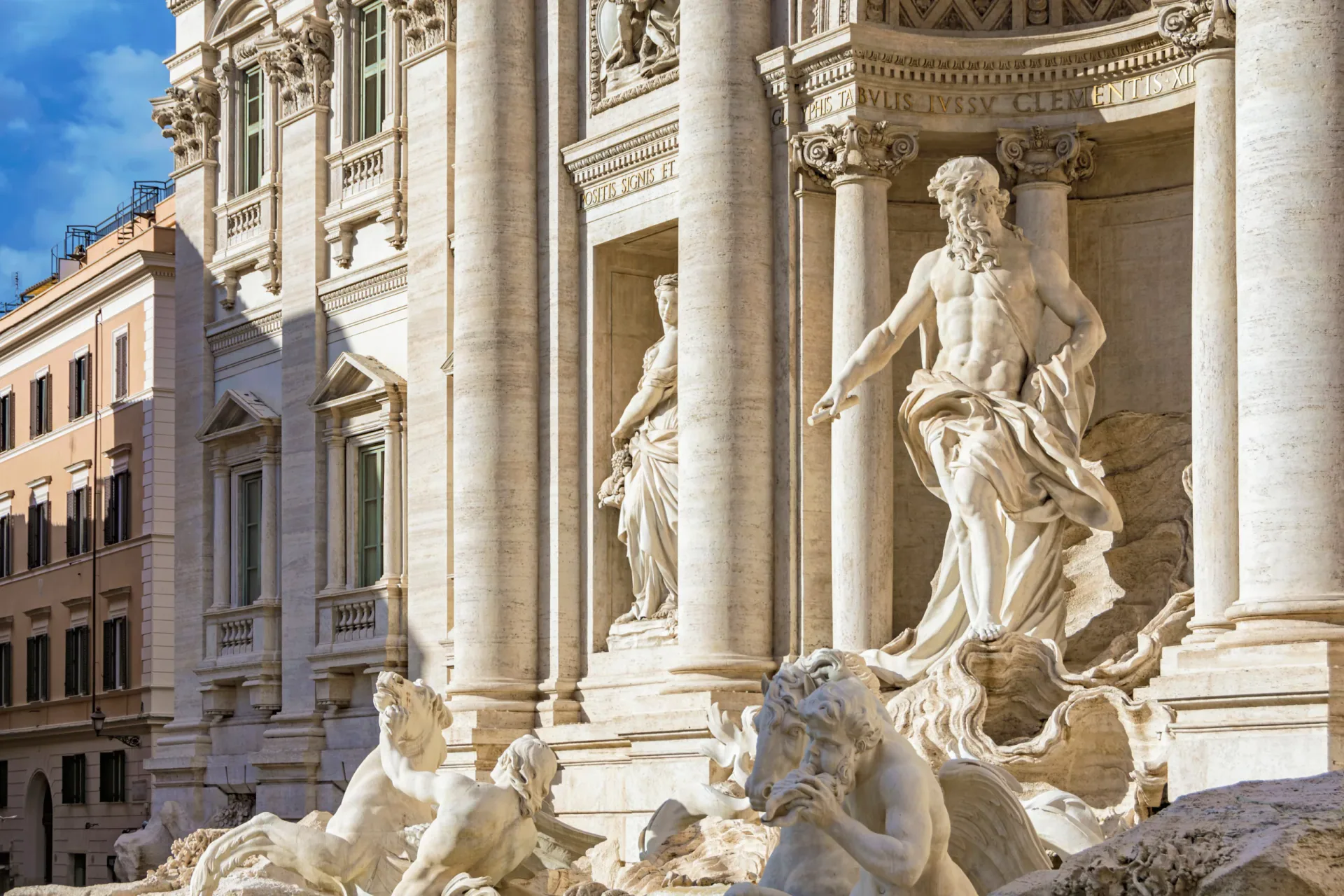 Close-up of the majestic marble statue of Oceanus standing in the central niche of the Trevi Fountain in Rome. Flanked by Corinthian columns and allegorical statues, with the Latin inscription of Pope Clement XII visible above.