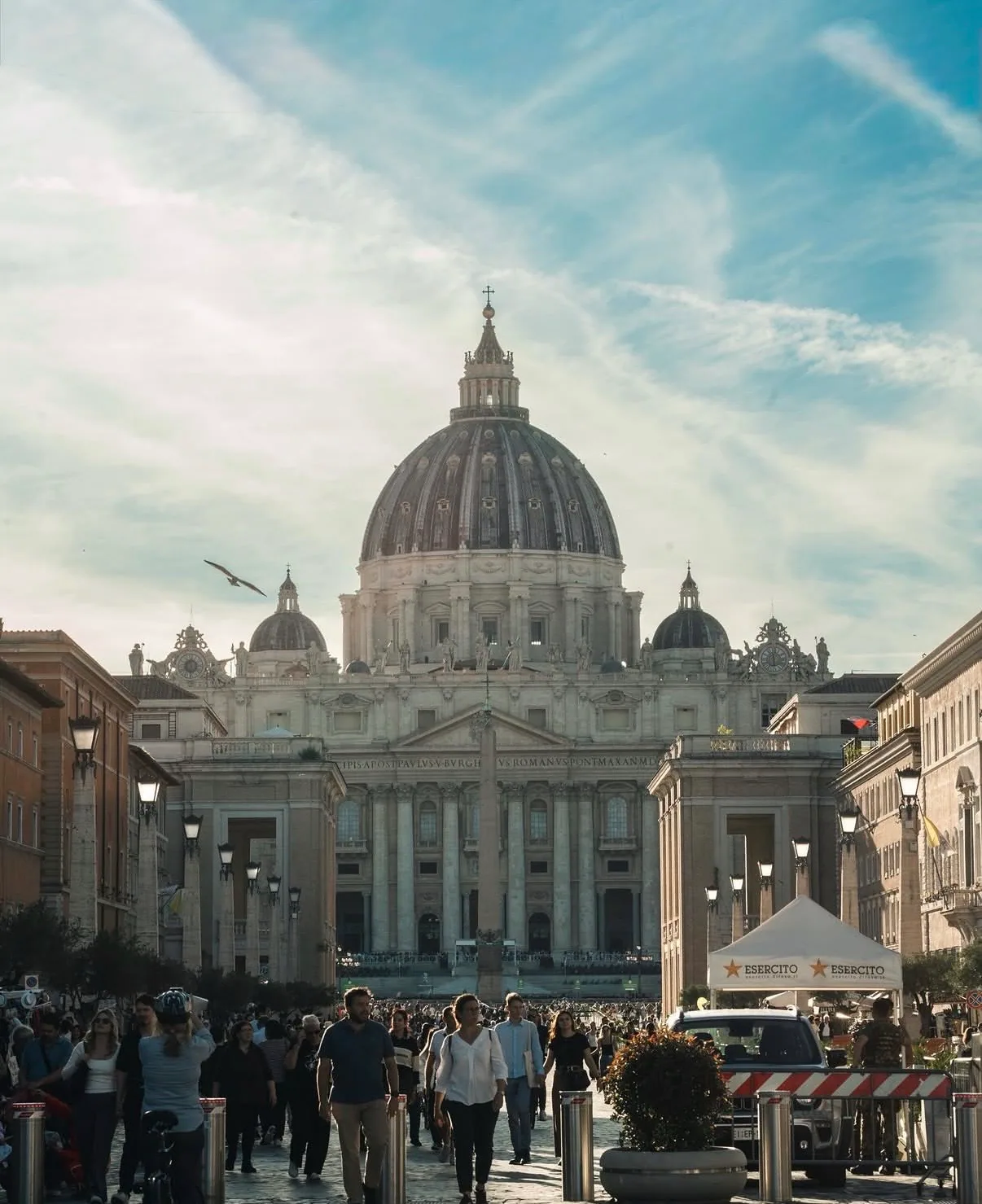 Via della Conciliazione leading towards St Peter's Basilica, its dome and colonnade ahead and people walking along the street.