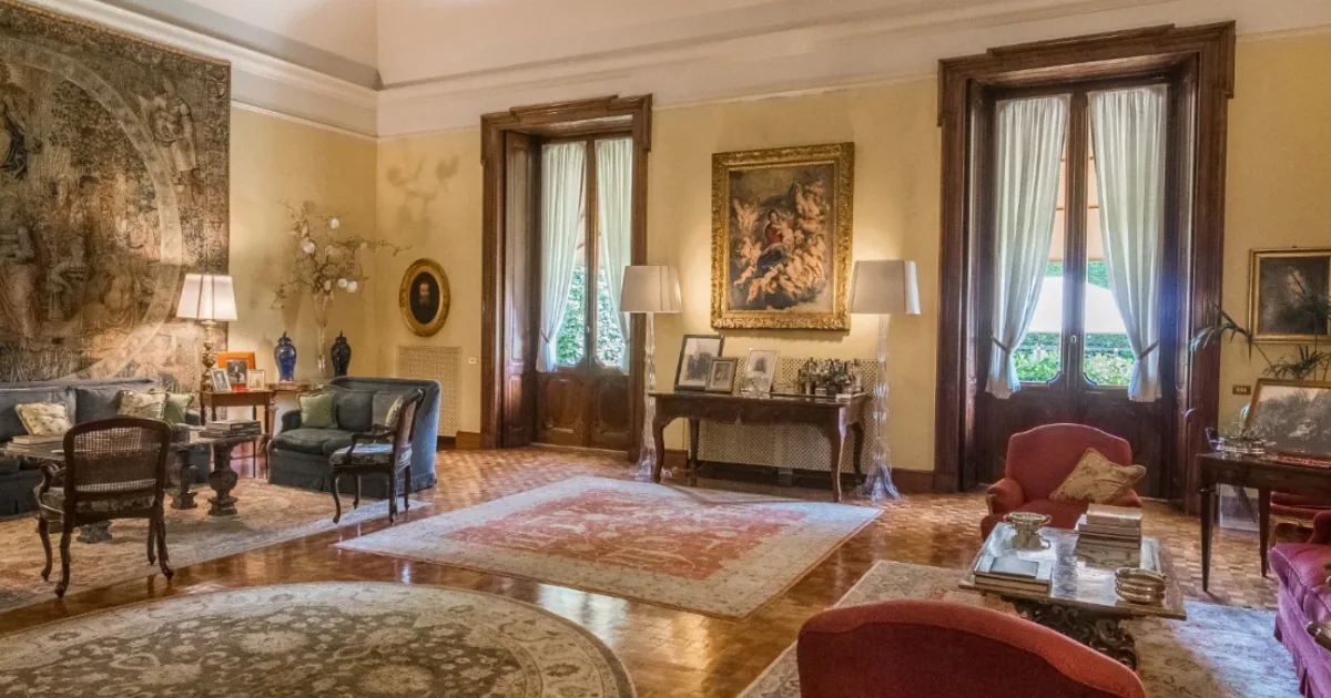 A salon at Villa Spalletti Trivelli in Rome, with a tapestry on the wall, family portraits, antique armchairs and tall windows opening onto the garden.