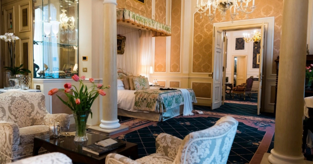 A salon at Villa Spalletti Trivelli in Rome, with a tapestry on the wall, family portraits, antique armchairs and tall windows opening onto the garden.
