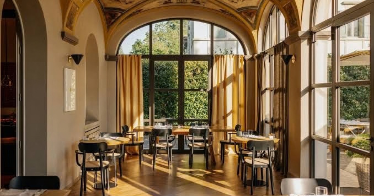 A contemporary room at The First Arte in Rome, with blue velvet armchairs, a striped rug and glass doors opening onto a private terrace.